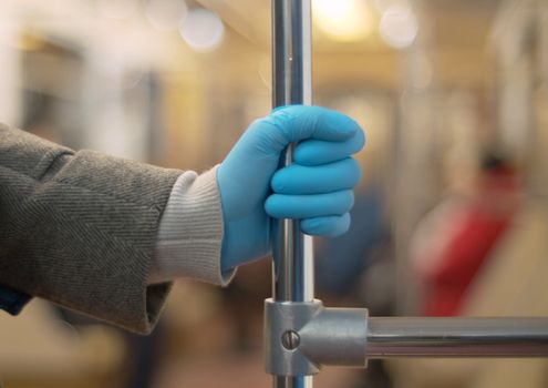 Close up female hand in protective blue glove holding metal stand in subway car. Coronavirus epidemic in the city. Healthy and safety lifestyle concept. Covid-19 pandemic