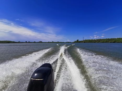 Wake leads water behind a speeding boat in a sunny day