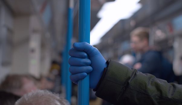 Close up hand in protective glove holds grab bar in subway car. Man in subway during coronavirus epidemic. Safety lifestyle concept. COVID-19 pandemic