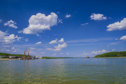 Summer scene on Danube river, shipyard with cranes and cargo ships on river.