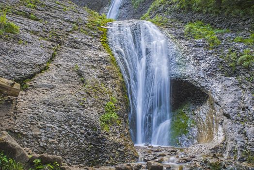 Water stream on stone wall in summer mountain