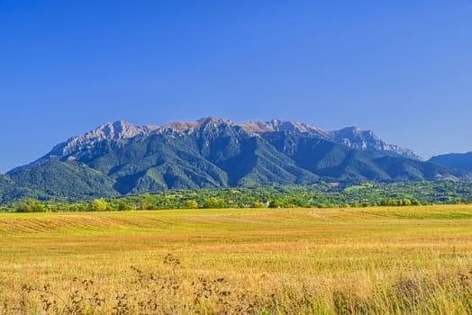 End of summer landscape in Romanian Carpathians: flat field, hill village, green forest and rocky alpine area.