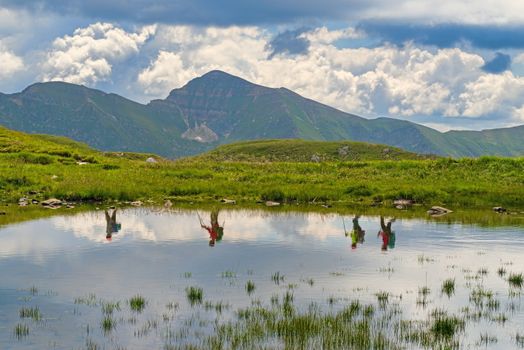 Summer mountain landscape, reflecting tourists in water, trekking travel concept