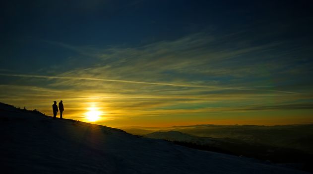 People silhouettes at sunset on winter mountain.