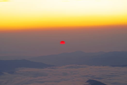 Red sun at sunrise from mountain top, low clouds and creast in valley