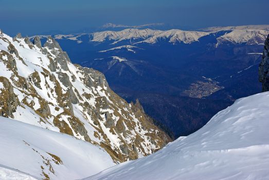 Winter mountain scene: snow covered rocks and sports resort to the valley