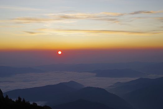 Sunrise landscape, sun appear at horizon over the crest, low clouds in the valley