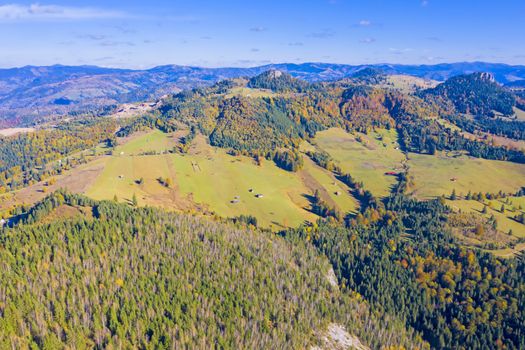 Aerial view of meadows and forest in autumn mountain landscape.
