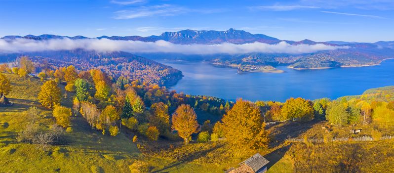 Autumn mountain panorama in Romanian Carpathians, mist cloud over the lake and colored trees, Bicaz Lake