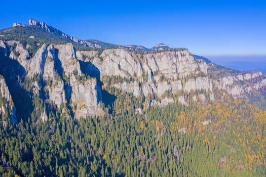 Aerial view of mountain rock wall and autumn forest in Romanian Carpathians.