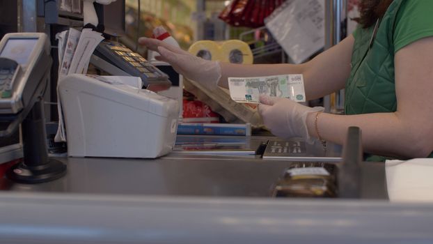 Close up checkout counter in the supermarket during coronavirus epidemic. Hands of cashier holding cash. Ccoronavirus epidemic