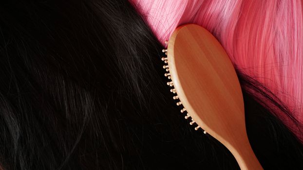 Pink and black wig with long hair and combs a wooden comb. Hairdresser and hair care