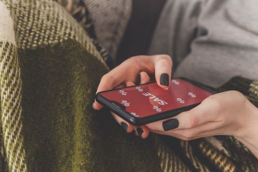 Sale on the phone screen. Woman holds a phone in his hand and sees the inscription sale. Online shopping without leaving home during quarantine. Black friday sale.