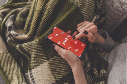 Sale on the phone screen. Woman holds a phone in his hand and sees the inscription sale. Online shopping without leaving home during quarantine. Black friday sale.