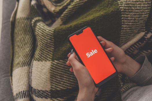 Sale on the phone screen. Woman holds a phone in his hand and sees the inscription sale. Online shopping without leaving home during quarantine. Black friday sale.