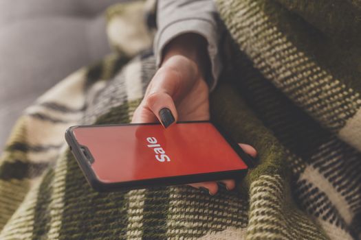 Sale on the phone screen. Woman holds a phone in his hand and sees the inscription sale. Online shopping without leaving home during quarantine. Black friday sale.