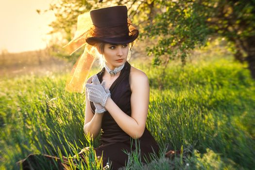 young blonde girl in a brown vintage dress and top hat reads a book in spring garden