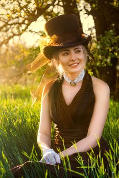 young blonde girl in a brown vintage dress and top hat in a feather grass