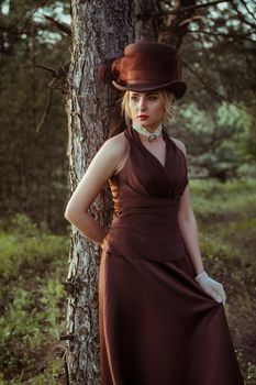 young blonde girl in a brown vintage dress and top hat in the forest