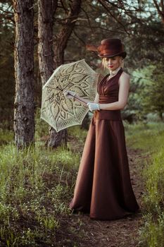 young blonde girl in a brown vintage dress and top hat in the forest