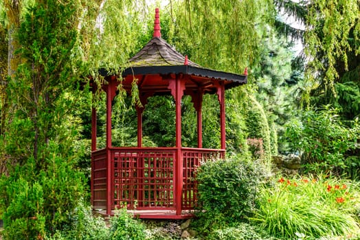 Stylish red pagoda in a Japanese garden among trees and green plants in sunny day.