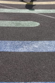 Walking man shadow on colored line shapes on asphalt surface texture.