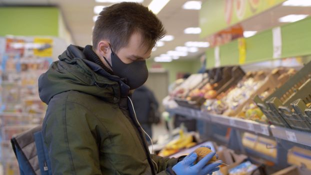 A man in a protective mask and gloves choosing kiwi in the supermarket. Coronavirus epidemic in the city. COVID-19 pandemic