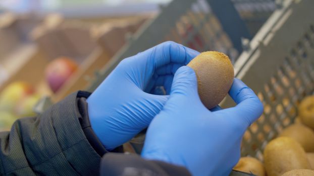 Close up hand of a man choosing kiwi fruits in the supermarket. Protective gloves. Coronavirus epidemic in the city. COVID-19 pandemic