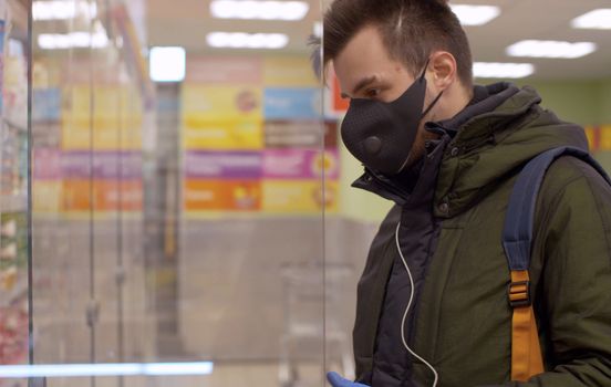 A man in a protective mask and gloves choosing food in the supermarket. Coronavirus epidemic in the city. COVID-19 pandemic