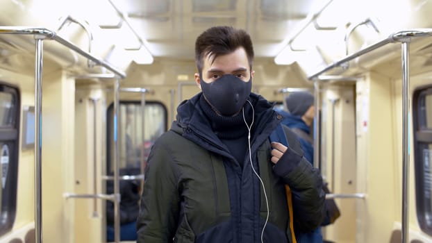 Close up portrait of a young man in reusable protective mask inside subway car. Blurry passengers. Coronavirus epidemic precautions. Healthy lifestyle concept. COVID-19 pandemic