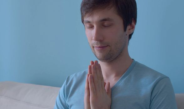 Portrait of young meditating man on blue background. Close up. The concept of meditation, relaxation, yoga, stress relief and inner peace and quiet