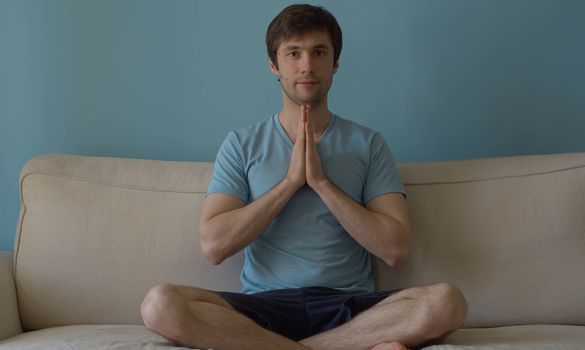 Portrait of young meditating man on blue background. The concept of meditation, relaxation, yoga, stress relief and inner peace and quiet