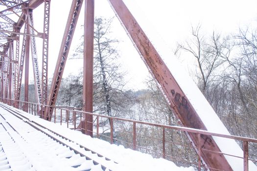 Winter landscape. Metall red bridge over the frozen river