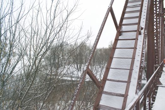 Winter landscape. Metall red bridge over the frozen river