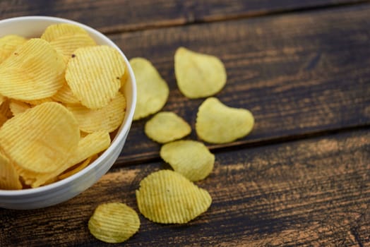 Crispy potato chips in a bowl on an old wooden vintage table.