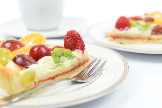 Conception of healthy fruit dessert - fresh homemade multi fruit tart on plates with cup of coffee in close-up.