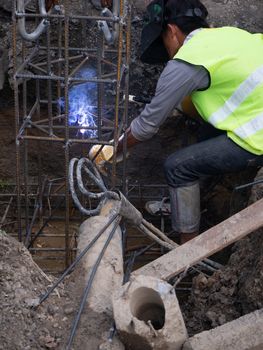 Worker in protective mask welding steel railings outdoors, sparks fly down