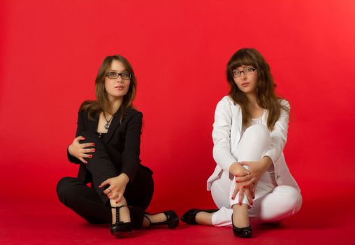 young pretty sisters twins posing sitting in studio on red background