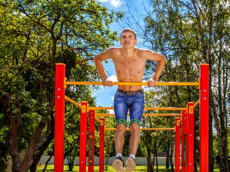 young man is practicing on a horizontal bar in the park on summer