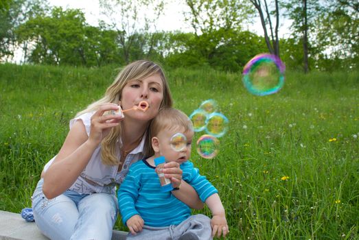 mother with her son blowing bubbles outside in city park on spring day