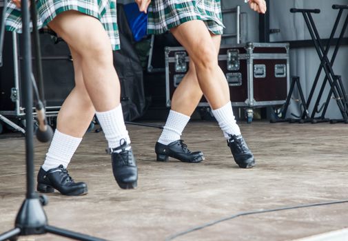 female legs of two irish dancers in green checkered dresses on the stage 