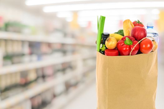 Grocery shopping concept image - Eco friendly paper shopping bag filled with various food products on  blurred supermarket background.