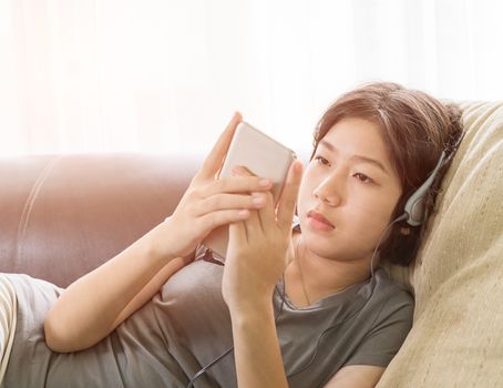 Close up young asian woman short hair listening music from mobile phone on the couch at home