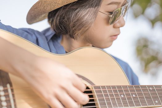 Close up young asian women short hair wear hat and sunglasses playing guitar in countryside Thailand