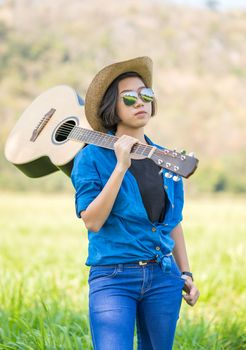Young asian woman short hair wear hat  and carry her guitar  in grass field countryside Thailand