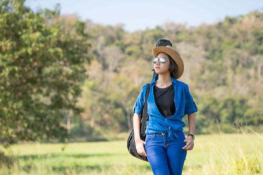 Young asian woman short hair wear hat walking and carry her guitar bag along in countryside Thailand