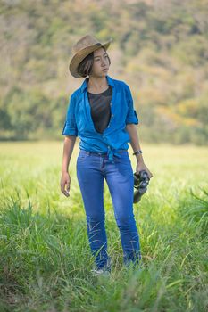 Young asian woman short hair wear hat and hold binocular in grass field countryside Thailand