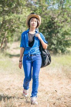 Young asian woman short hair wear hat walking and carry her guitar bag along in countryside Thailand