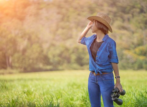 Young asian woman short hair wear hat and hold binocular in grass field countryside Thailand