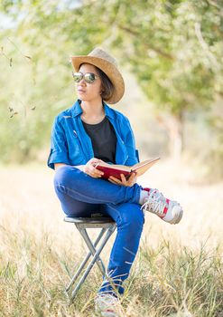 Young asian women short hair wear hat and sunglasses read a book ,sit on chair in countryside Thailand